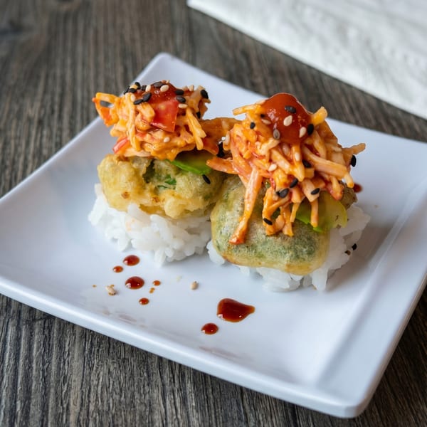 Two pieces of fried sushi topped with spicy crab salad and sesame seeds on a white plate.