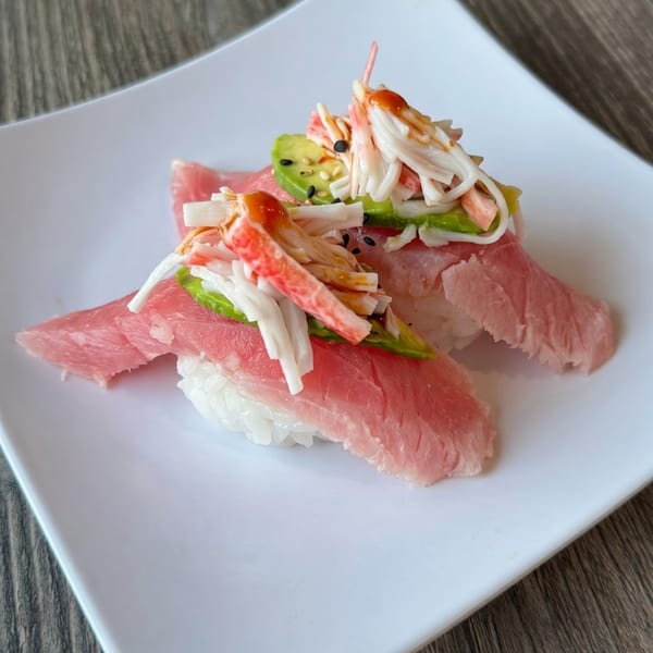 Two pieces of tuna nigiri topped with crab, avocado, sesame seeds, and a drizzle of sauce.