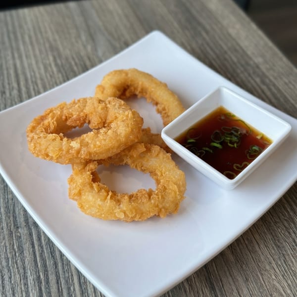 Crispy golden onion rings on a white rectangular plate with a side of dark dipping sauce.