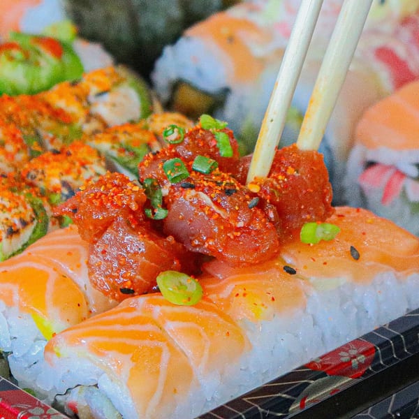 Chopsticks picking up a piece of spicy tuna sushi roll with salmon, green onions, and sesame seeds.