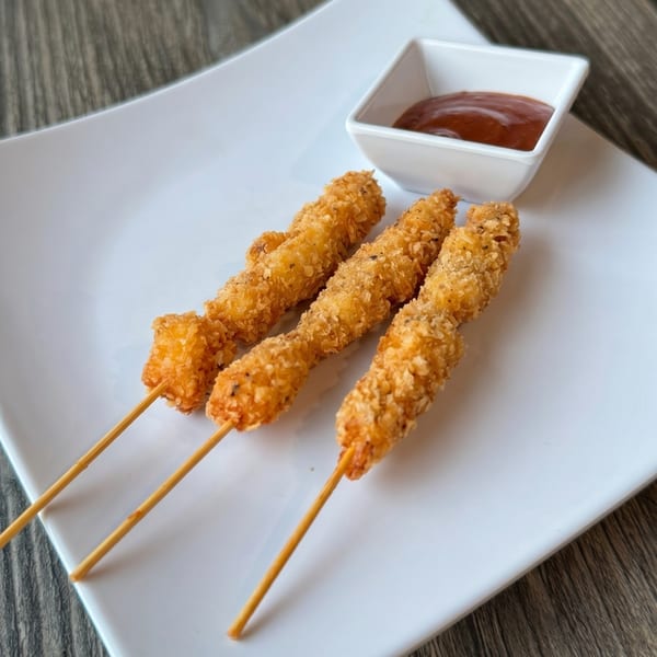 Three crispy fried chicken skewers with a side of dipping sauce on a white plate.