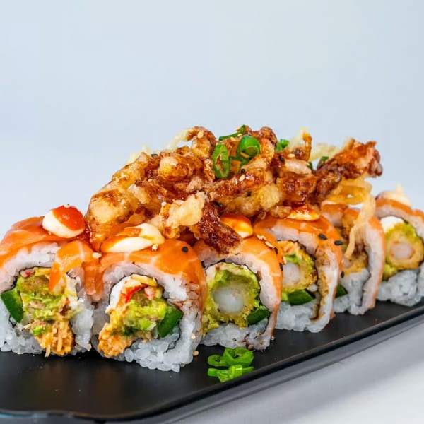 Sushi rolls with salmon, avocado, shrimp tempura, and crispy fried onions on a black plate.