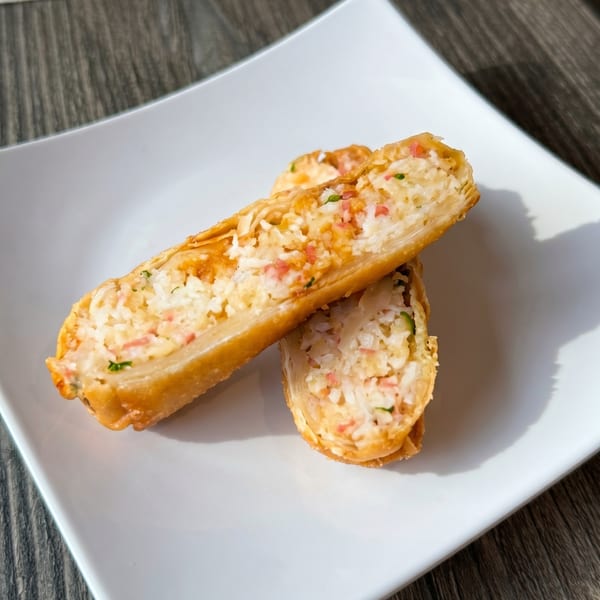 Two golden-brown fried spring rolls, cut in half, revealing a filling of rice, crab, and green onions.