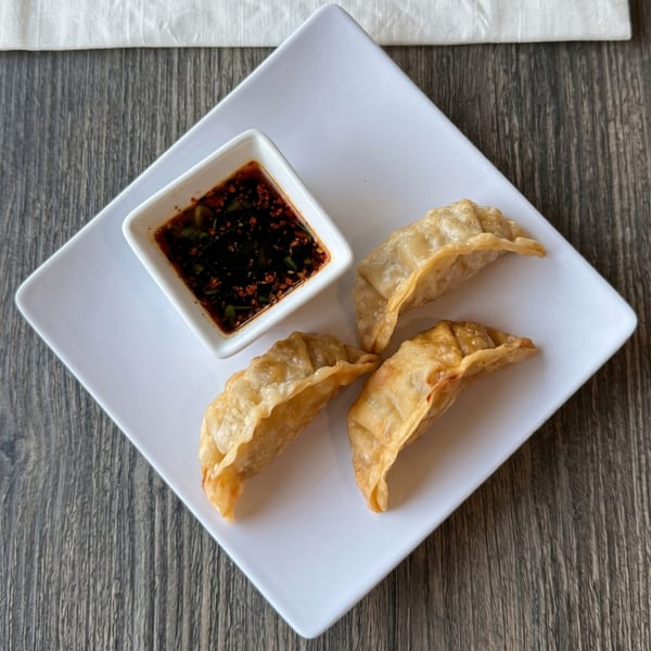 Three golden-brown fried dumplings and a small dish of dark dipping sauce on a white square plate.