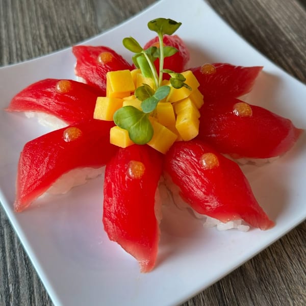 Red tuna nigiri sushi with mango cubes and microgreens arranged like a flower on a white plate.