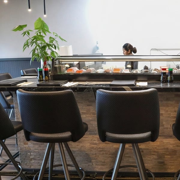 A sushi bar with a chef preparing food, bar stools, and a plant on the counter.