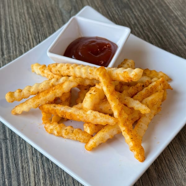 Crispy seasoned crinkle-cut fries with a side of ketchup on a white rectangular plate.